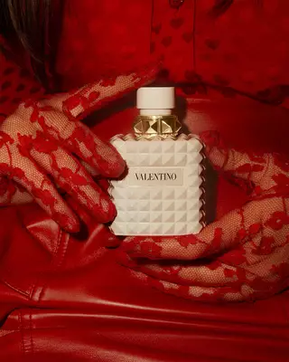 Eine Frau in Rot, die exquisit verzierte rote Spitzenhandschuhe tragt, halt BORN IN ROMA IVORY DONNA in der Hand.