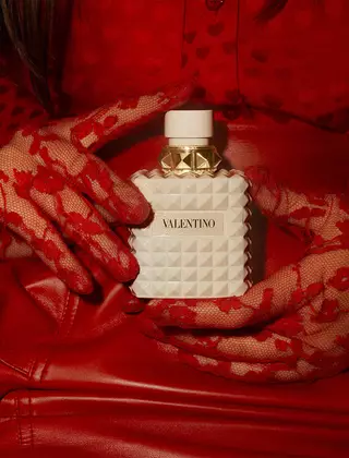 Eine Frau in Rot, die exquisit verzierte rote Spitzenhandschuhe tragt, halt BORN IN ROMA IVORY DONNA in der Hand.